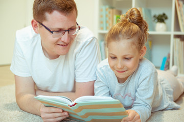 Young happy father reading book with  cute daughter at home