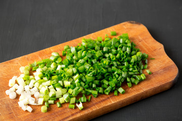 Chopped green onions on a rustic wooden board on a black background, side view. Close-up.