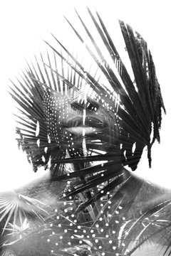 Double exposure of a dark skinned man with dreadlocks and face paint combined with a photograph of a beautiful lush plants in black and white