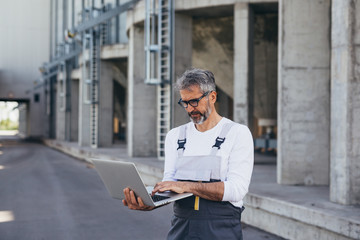 worker using laptop , grain silo in blurred background