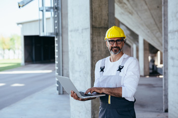 worker in protective wear using laptop on construction site