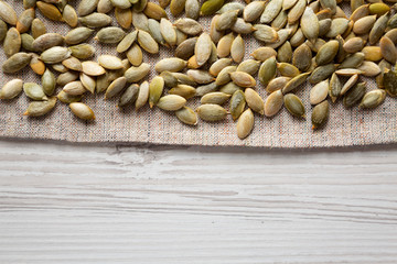 Roasted pumpkin seeds on cloth over white wooden background, top view. Flat lay, overhead, from above. Copy space.