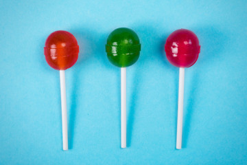 Three lollipops on a stick, at the white pastel background, the view from above.