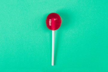 A red lollipop on a stick at the green background, a view from above, sweets and caramel.