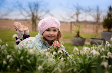 Little girl in hat lying beside snowdrops smiling
