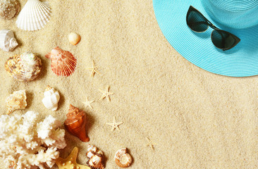 Hat and sunglasses on the sandy beach with seashells. Summer background