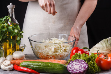 A young woman in a gray apron sipes a salad of Chinese cabbage