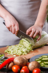 A young woman in a gray apron cuts chinese cabbage