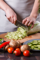A young woman in a gray apron cuts chinese cabbage