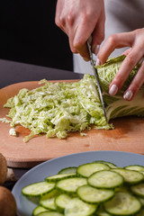 A young woman in a gray apron cuts chinese cabbage
