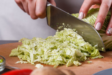 A young woman in a gray apron cuts chinese cabbage