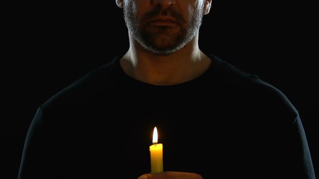 Man from religious sect holding candle against black background, spirituality