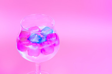 A cold drink with colorful pink and blue ice in a wine glass on a soft pink background. Summer concept image with copy space for text