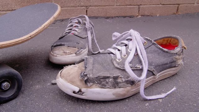 ECU SLIDER SHOT PAST A SKATEBOARD TO A PAIR OF WORN OUT SKATE SHOES.  IN 4K.  NO PEOPLE.