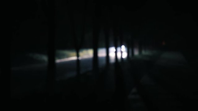 blurred night footage of car riding on the street in the darkness. Car headlights illuminate the street at night. Dark urban background