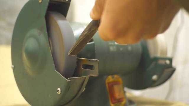 A chisel is producing sparks by touching a spinning sharpening stone while is sharpened. Sharpening a chisel on grinding machine with sparks fly