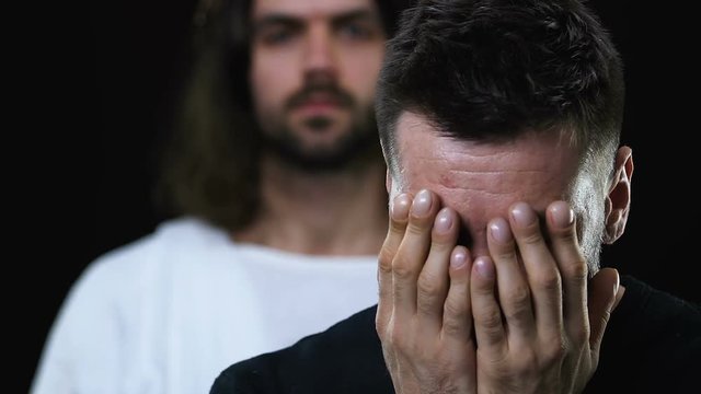 Jesus Christ healing sick crying man, closing face with hands, dark background