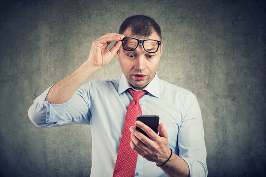 Businessman in eyeglasses watching smartphone in shock reading message
