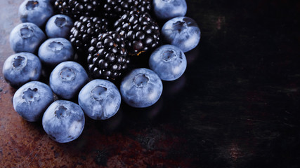 Blueberries and blackberries on dark background. Fresh berries for vegan. Assorted berries on rusty background. Flat lay