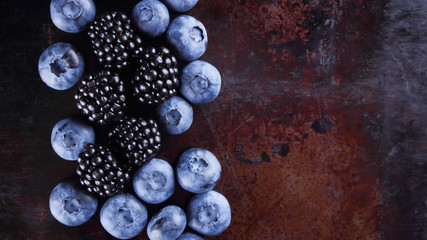 Blueberries and blackberries on dark background. Fresh berries for vegan. Assorted berries on rusty background. Flat lay
