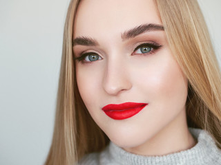 Fototapeta na wymiar Closeup natural light beauty portrait of smiling blonde woman model with vibrant saturated red lips bright lips makeup, cheekbones and healthy shiny skin.