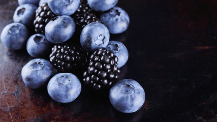 Blueberries and blackberries on dark background. Fresh berries for vegan. Assorted berries on rusty background. Flat lay