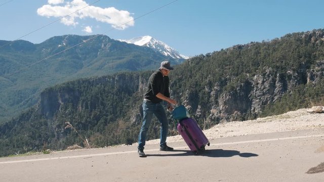 Young man with purple suitcase hitchhiking on sunny day