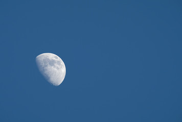 A crescent moon being visible in daytime.  Ridding in Eastern sky, hanging high, a pale impression against a background of beautiful clear blue sky.