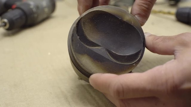 A mechanic is holding a spent car piston and examining rings. Close-up. Car service, repair, maintenance and people concept