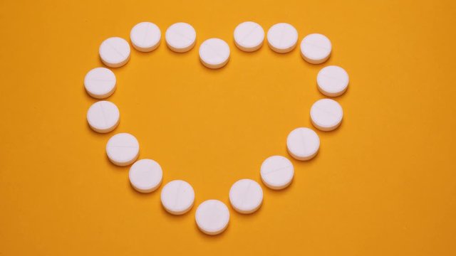 Heart from pills. Stopmotion of pills on yellow background. Making the shape of heart