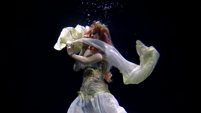 underwater shooting of woman in evening dress floating in big aquarium with black background