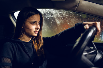 Young woman holding a car driving wheel in a rainy night rain