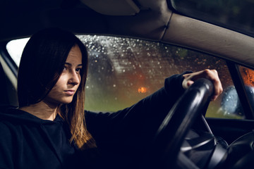 Young woman holding a car driving wheel in a rainy night rain