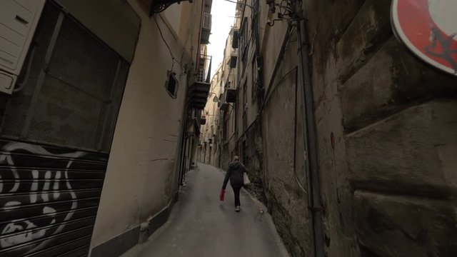 Steadicam POV shot of walking along the narrow alleyway with shabby houses walls and following unidentified woman. Palermo, Italy