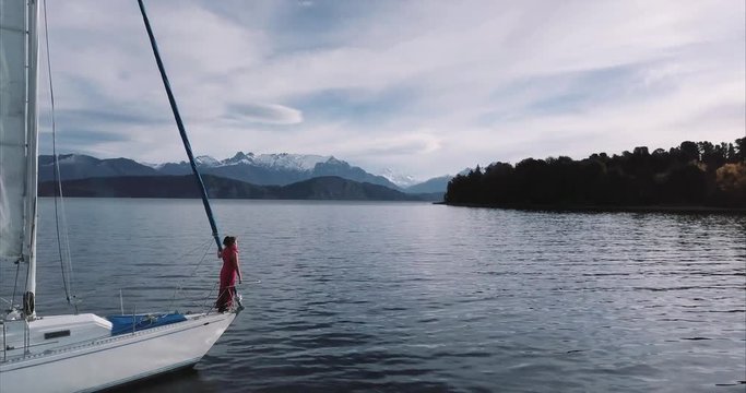 Aerial view of a Hispanic woman relaxing on the bow of the sailboat looking at the beautiful Patagonian lake Nahuel Huapi. 4k		