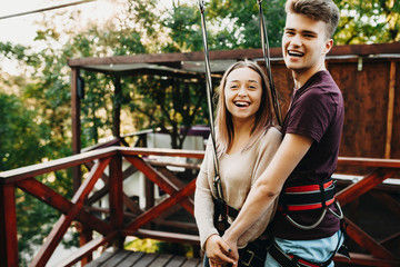 Amazing young couple having fun laughing while looking at camera being equipped before zipline trip while traveling.