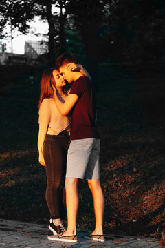 Full lenght portrait of a audlt caucasian couple embraicing while dating outside in sunset light.