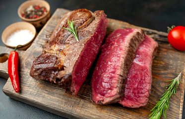 Grilled rib eye beef steak with herbs and spices on a stone background