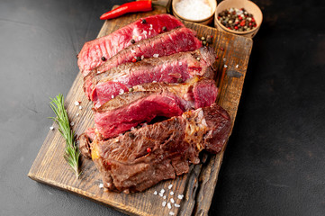 Grilled rib eye beef steak with herbs and spices on a stone background