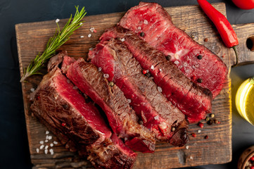 Grilled rib eye beef steak with herbs and spices on a stone background