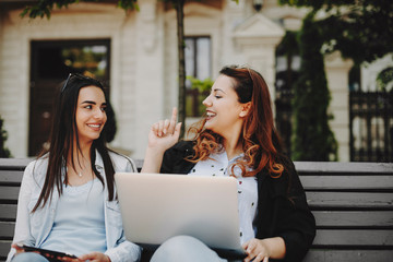 Cute plus size girl with red hair speaking with her girlfriend while showing something with a finger while another is looking smiling her against a building.