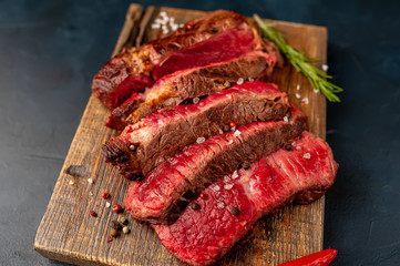 Grilled rib eye beef steak with herbs and spices on a stone background