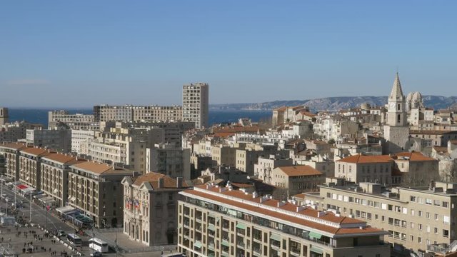 Cityscape of Marseille with lively street, houses, bell tower of Notre Dame des Accoules Church and sea in background. France