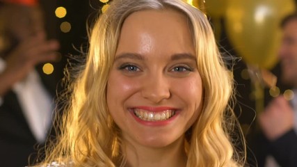Cheerful smiling lady blowing on confetti and making air kiss at birthday party