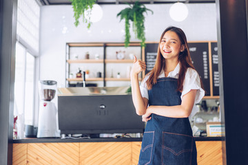 Pretty young asian waitress standing arms crossed in cafeteria.Coffee Business owner Concept.  barista in apron smiling at camera in coffee shop counter