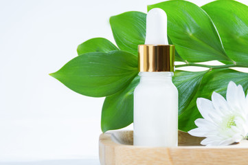 Natural cosmetics: serum with dropper, white flower and green leaves on white background.