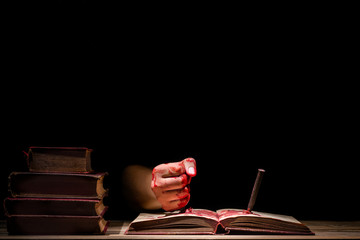 bloody hand stab an old book with pin or nail, horror concept