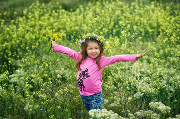 Portrait of a beautiful little girl in a wreath of wild flowers . Children on a walk