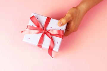 Male hand holding gift box with ribbon on pink background, top view