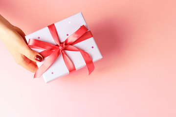 Female hand holding gift box with ribbon on pink background, top view